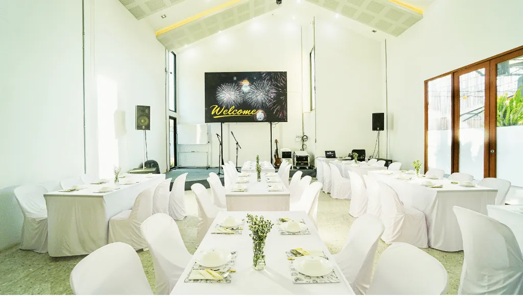 โถงจัดเลี้ยงเพดานสูงของ COME Catering ขอนแก่น จัดโต๊ะสีขาวพร้อมเวทีและจอ LED